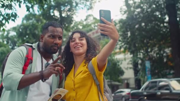 ベトナムのストリートでスマートフォンでセルフィーを取る若い多様なカップルのミディアムショット ガジェットと笑顔を保持し インドの男性がVサインを表示し 面白い顔を作る — ストック動画