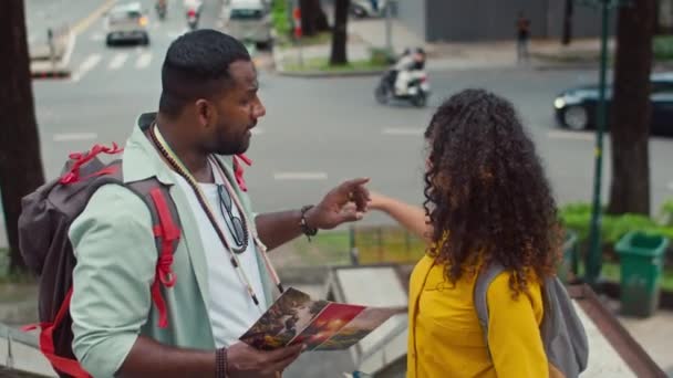 アフリカ系アメリカ人男性と白人女性のミディアムショットは 忙しい通りの歩行者橋の上に立って 観光パンフレットを見て 新しい都市を探索しながら次の目的地を議論します — ストック動画