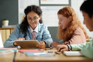 Kültürler arası iki tatlı kız İngilizce kelime ya da yeni dil bilgisi kurallarının sunumunu hazırlarken biri alet ekranına dokunuyor.