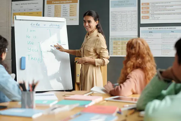 Happy Young Brunette Teacher Pointing Whiteboard Pronouns While Explaining Present — Stock Photo, Image
