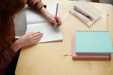 Ortaokul öğrencisinin el açısının üstünde, İngilizce dil bilgisi dersinde masa başında otururken kalemle çizim yapıyor.