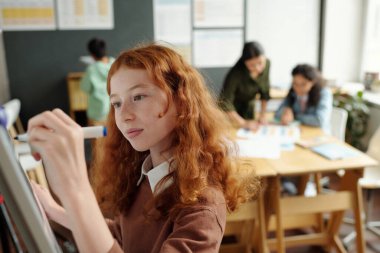 Sınıf arkadaşları ve öğretmenlere karşı sunum hazırlarken beyaz tahtaya dil bilgisi kuralları yazan sevimli liseli kıza odaklan