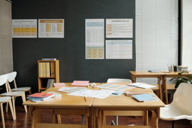 Ahşap masa üzerinde doküman ve fotokopi kitapları olan İngilizce sınıfındaki hiç kimse gramer tabloları olan duvara karşı duramaz.