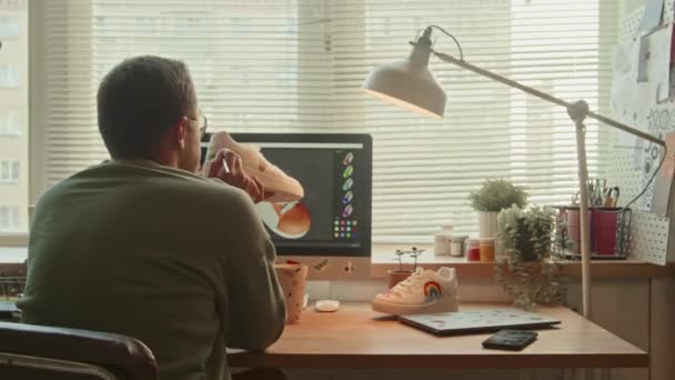 新しいアイテムをカスタマイズする画面上のカラフルなスケッチでコンピュータの前に座っている男性のスニーカーデザイナーのバックビュー — ストック動画