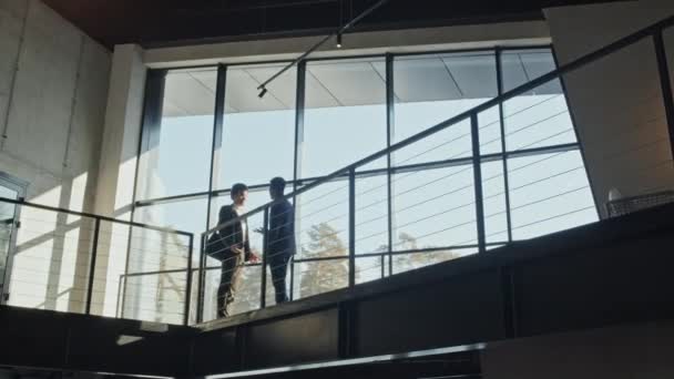 两个身穿西服的年轻多民族商人站在高大的窗前的大写字楼大堂里 互相问候 拍了一张大大的低角度照片 — 图库视频影像