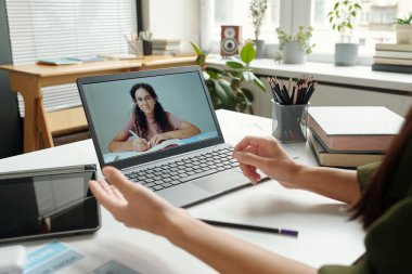 Dizüstü bilgisayar ekranında, dil bilgisi kuralını açıklayan ve online ders sırasında onu dinleyen zeki çoklu etnik kız öğrenci.