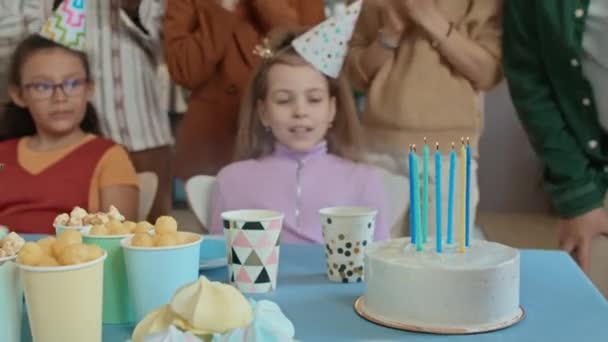 中特写镜头 一个无法辨认的孩子在生日蛋糕上吹灭蜡烛 两个未成年少女在一旁看着 拍手拍手 匿名父母在背景中欢呼雀跃 — 图库视频影像