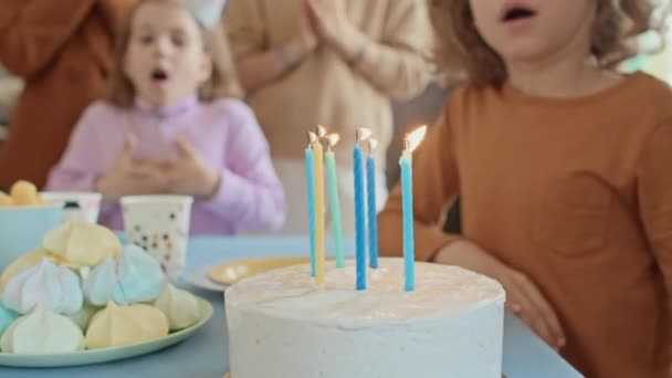 子供の誕生日のケーキにろうそくを吹き飛ばし 子供のパーティーでスイーツと一緒にテーブルに座っている間 認識できない子供のクローズアップ選択的な焦点ショット — ストック動画