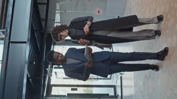 タブレットコンピュータを搭載した若いアフリカ系アメリカ人ジュニア企業の従業員の完全な垂直スローモショットは 問題を議論する方法についてコーカサス女性の同僚と話しています — ストック動画