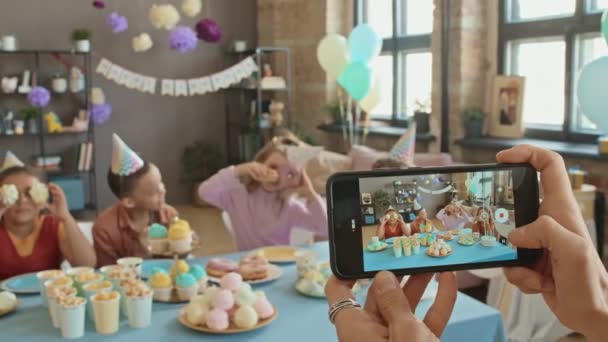 特写有选择性地拍摄了一些照片 照片中的一些匿名女性手持智能手机 带着糖果坐在桌旁 在生日派对上玩得很开心 到处鬼混 拍了很多小孩的照片或录像 — 图库视频影像
