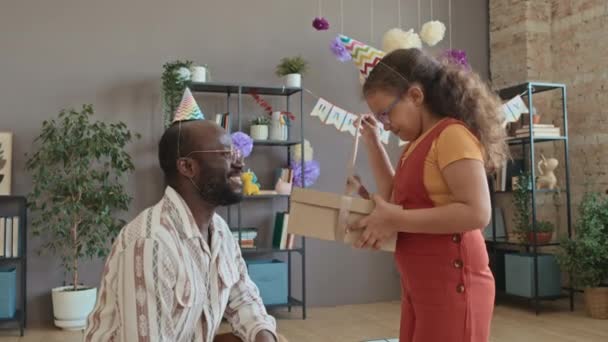 中等比例的非洲裔美国爸爸送给9岁女儿的生日礼物 女孩拉带子 打开盒子 拿出新耳机 他们都在微笑 拥抱和亲吻 — 图库视频影像