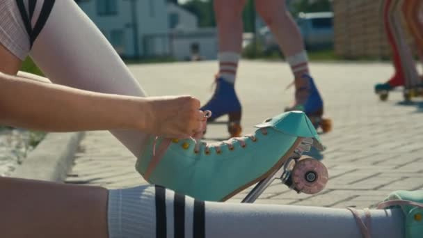 昼間は屋外でローラースケートのレースを締める地面に座っている若い白人少女の中型傾斜ショット — ストック動画