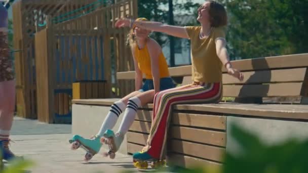 两个年轻的女性朋友坐在外面的长椅上 一个女孩抱着她们走过来 个个面带笑容 — 图库视频影像