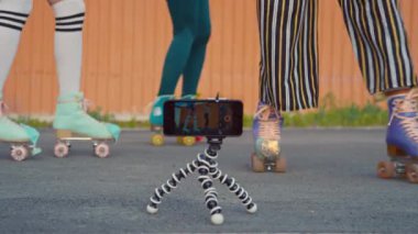 Üç kadın arkadaşın gündüz vakti kapsülün üzerinde akıllı telefonla yatay video çekerken eş zamanlı hareketler yaptığı orta seviye bir çekim.