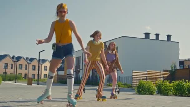 カラフルなヴィンテージ服 ヘッドフォン ローラーのスケートを着た3人の白人少女のスローモートショットは 昼間に公園で乗り始める — ストック動画