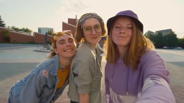 3人の陽気な明るい十代の女の子がカメラを見て 笑顔で ポーズをし 昼間通りに外でセルフィーを撮った中型ショット — ストック動画