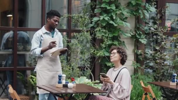 아프리카계 미국인 웨이터의 낮에는 야외에서 메뉴에서 식사를 선택하는 즐거운 코카서스 — 비디오