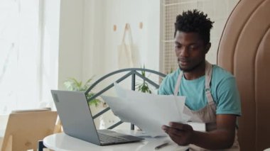 Orta boy erkek Afro-Amerikan kafe çalışanı gündüz vakti masada oturmuş evrak işleriyle uğraşıyor.