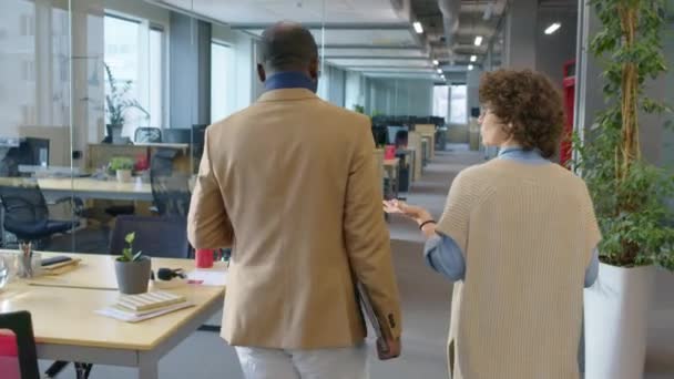 男性アフリカ系アメリカ人女性コーカサス人労働者のバックビュー追跡ショットは 昼間の活発な会話を持つオフィスに沿って歩いています — ストック動画