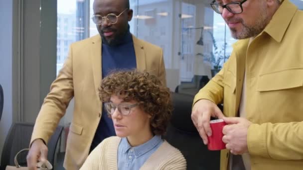 昼間のオフィスの多様な男性同僚にプロジェクトを説明する机に座っている白人女性マネージャーのティルトショット — ストック動画