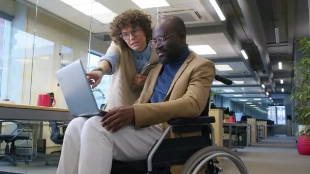車椅子の男性アフリカ系アメリカ人の従業員の低い角度は 昼間の女性の白人同僚にプロジェクトのアイデアを示しています — ストック動画