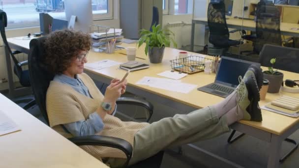 アークショット 笑顔の女性コーカサスマネージャーがオープンスペースオフィスの机に座って 昼間スマートフォンで休憩してチャット — ストック動画