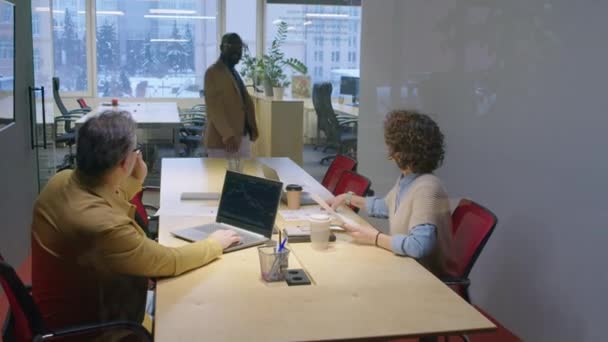 陽気なアフリカ系アメリカ人の男性マネージャーが昼間のガラス壁の後ろのオフィスボードルームでコーカサス人の同僚と会うために来る — ストック動画