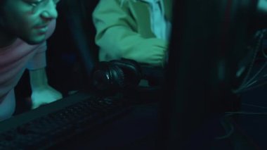 Ortadoğulu genç bir oyuncunun sanal kulüpte sandalyeye oturup online nişancı oyununa girmeden önce mikrofonla kulaklık taktığı orta ölçekli yakın plan bir fotoğraf.