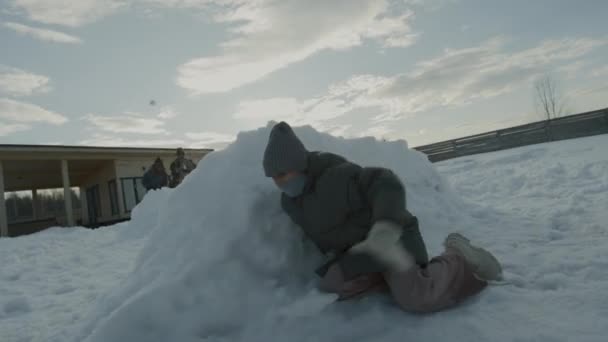 紧跟在后面的是身穿保暖外套头戴帽子的少女 她躲在雪墙后面 躲避朋友们扔雪球 然后逃离敌人 被追捕 落在厚厚的雪地里 — 图库视频影像