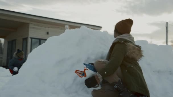 友人と遊んでいる間 雪のバリケードの背後で曲がっている10代のアフリカ系アメリカ人の少女のミディアムショット おもちゃ銃をロードし 敵の位置でスノーボールを撮影 — ストック動画