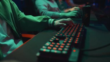 Klavyedeki tuşlara basan ve karanlık siber kulüpte oyun oynarken bilgisayar faresini manipüle eden tanınmayan gençlerin yakın çekim görüntüleri.