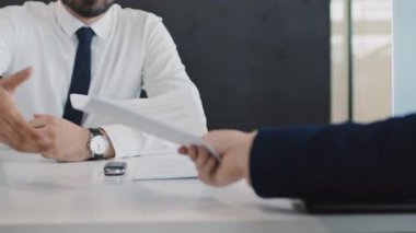 Tanımlanamayan oto satış temsilcisinin, imzalı araba satışı sözleşmesini imzalanan isimsiz bir erkek alıcıdan geri alırken ve ona yeni bir aracın elektronik anahtarını verirken yakın plan çekimi.