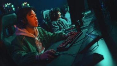 Orta ölçekli kulaklıklı Çinli oyuncu ve çok uluslu takım arkadaşlarının FPS oyun turnuvasını kazanırken, tezahürat yaparken, boğmaca atarken ve beşlik çakarak kutlarken.