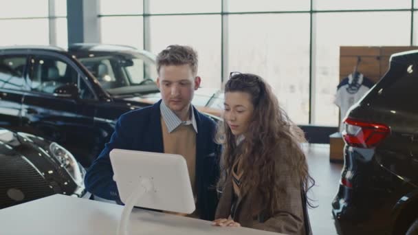 中等比例的白人青年男女站在汽车展示室里 观看数字平板电脑上的信息 比较汽车模型并查看贷款选项 — 图库视频影像