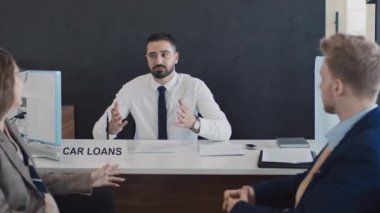 Genç Arap satış müdürünün araba galerisinde oturduğu orta boy bir fotoğraf. Beyaz karı ve kocayla kredi sözleşmesi şartları ve sigorta pazarlığı yapıyor.