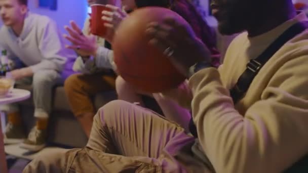ワクワクする若いアフリカ系アメリカ人男性のクローズアップスロームショットは バスケットボールで遊んで 自宅で友人とテレビでスポーツマッチを見ながら — ストック動画