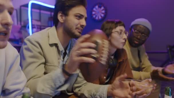 上周五晚 四个多民族朋友坐在沙发上 一边看体育比赛 一边喝啤酒 一边欢呼和评论 还有一个阿拉伯人玩橄榄球 — 图库视频影像