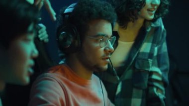 Siber kulüpte oturan, video oyunu oynayan ve kazanan, çok ırklı arkadaşların izlediği, tezahürat yaptığı, işaret ettiği ve sonra da beşlik çaktığı orta boy yakın plan bir Arap fotoğrafı.