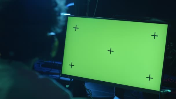 留著卷发的匿名顾客的特写镜头 在电脑上玩电脑游戏的耳机 网吧里有绿色的色键屏幕 转过头去说话 复制空间 — 图库视频影像