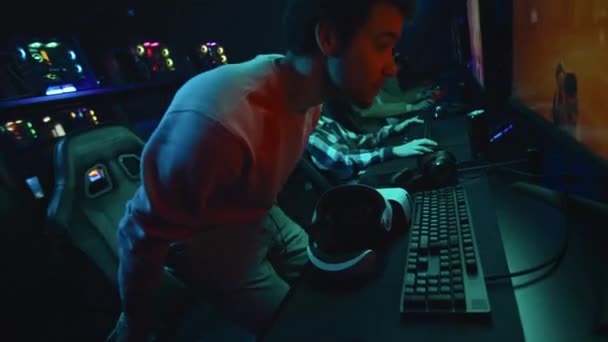 在繁忙的网络俱乐部里 坐在电脑前 戴上Vr耳机 准备在扩大的现实中玩第一人称射击多人游戏的阿拉伯年轻人的中景照片 — 图库视频影像