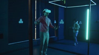 VR kulaklıklı iki genç adamın, boş karanlık arenada, üç boyutlu simülasyonlar yaparak, mavi neon ışıklarıyla arttırılmış gerçeklik oyunları oynamalarının tam karesi.