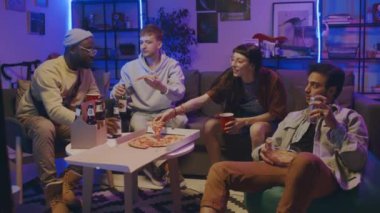Çok ırklı dört genç erkek ve kadının günlük kıyafetlerini giyip mavi neon ışıkta öğrenci evindeki partide birlikte oturdukları, pizza yedikleri, bira içtikleri ve sohbet ettikleri bir sahne.