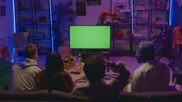四个多种族朋友坐在沙发上 与披萨和啤酒一起坐在黑暗的房间里 观看电视节目或电影 指着空白的绿色屏幕 复制空间 — 图库视频影像