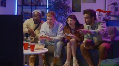 Dört mutlu çokkültürlü gencin evlerindeki mavi ışıkta televizyon karşısında oturduğu, kablosuz kontrolörlerle bilgisayar oyunu oynadığı, tezahürat yaptığı ve güldüğü bir sahne.