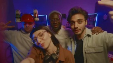 Neon ışıkları altında öğrenci evindeki partilerde sosyal ağlarda haber için akıllı telefondan video çeken dört genç arkadaşın orta boy selfie çekimi, maskaralık, gülümseme ve konuşma.