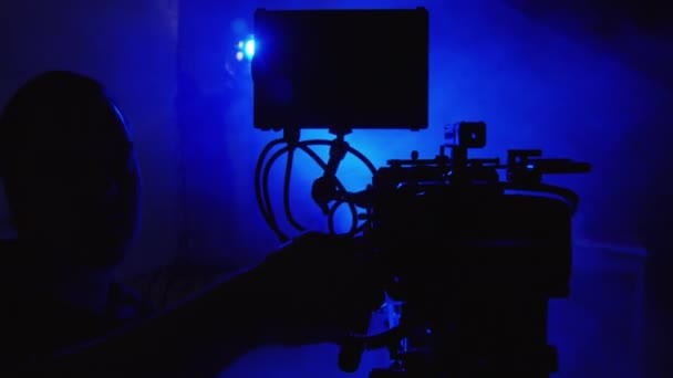 ダークスタジオでビデオ撮影のための装置を準備する生産技術者のクローズアップショット カメラをセットアップし ケーブルを差し込むカメラマン ブルーランプを設定する照明エンジニア — ストック動画