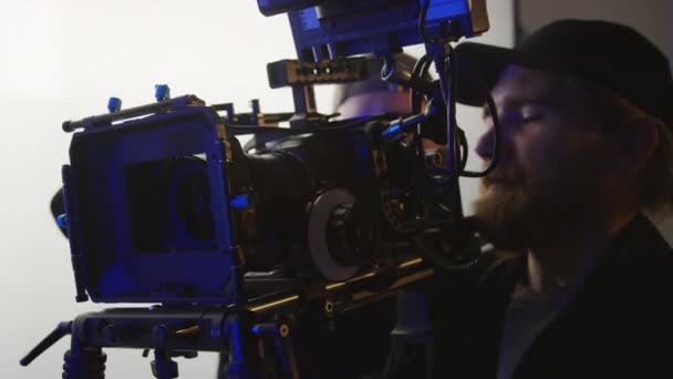 スタジオで撮影する準備をしている間 アシスタントに設定を調整しているアシスタントに指示を与える ビデオカメラまたは肩にカムコーダーを保持している白人男性のビデオグラファーのクローズアップショット — ストック動画