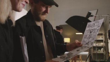 Erkek yönetmen ve kadın yapımcının stüdyodaki bilgisayar ekranında film çekimini tartışırken ve senaryo panosuna bakarken, video yönetmeni ve model çekimlere hazırlanırken orta ölçekli yakın çekim görüntüleri.