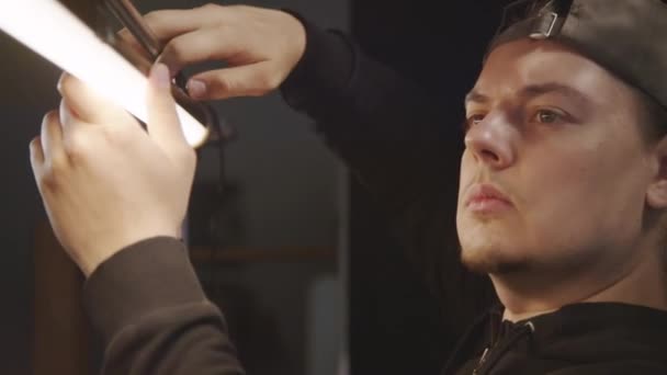 年轻的白人男性光技师安装水平灯和固定螺钉 同时准备在演播室拍摄的脸和手的特写 — 图库视频影像