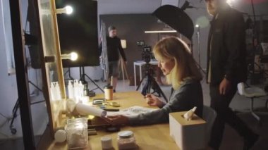 Prodüksiyon stüdyosundaki kadın yapımcının, reklam için senaryo ve senaryoya bakarken, erkek kameramanla konuşurken, stüdyoda çekim yapmaya hazırlanırken orta ölçekli bir görüntüsü.